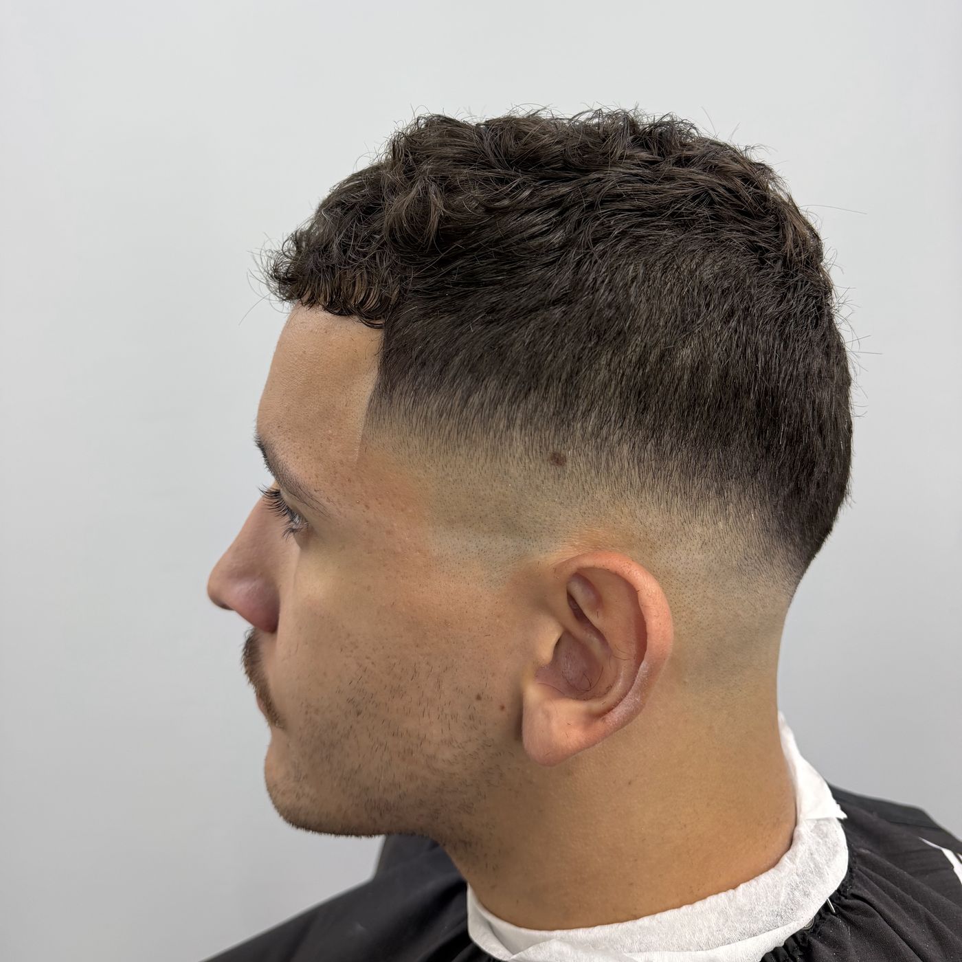 High drop fade with a curly textured crop, left profile